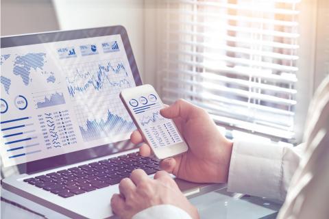 Business person viewing a computer and mobile phone, both with dashboards displaying graphs and charts